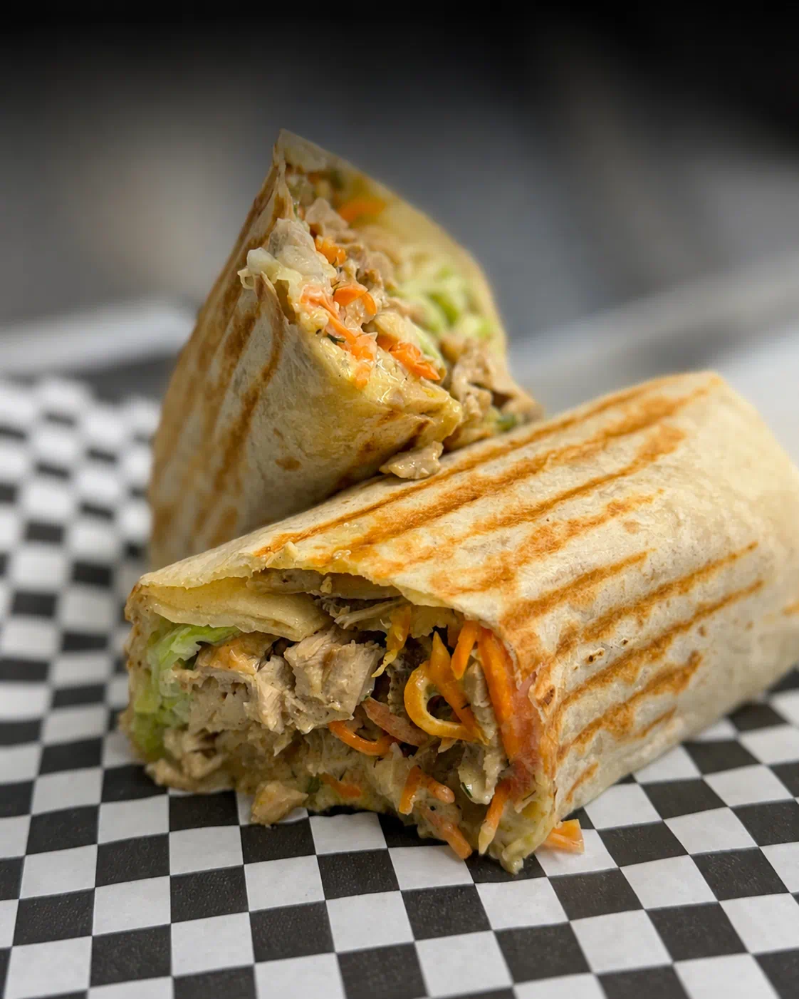 Kebab Grill shawarma wrap sliced in half on checkered paper, packed with chicken, pickled carrot and cabbage